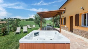 Ein Whirlpool in einem überdachten Außenbereich mit Patio-Tisch und -Stühlen, einer Holzpergola und Blick auf eine grüne Landschaft.