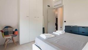 Ein modernes Schlafzimmer mit einem großen Bett, einem Kleiderschrank, einem Sessel und einem Schreibtisch.