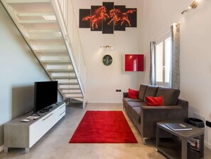Uma sala de estar moderna com escada, televisão de tela plana, sofá cinza, almofadas vermelhas, tapete vermelho e um relógio de parede.