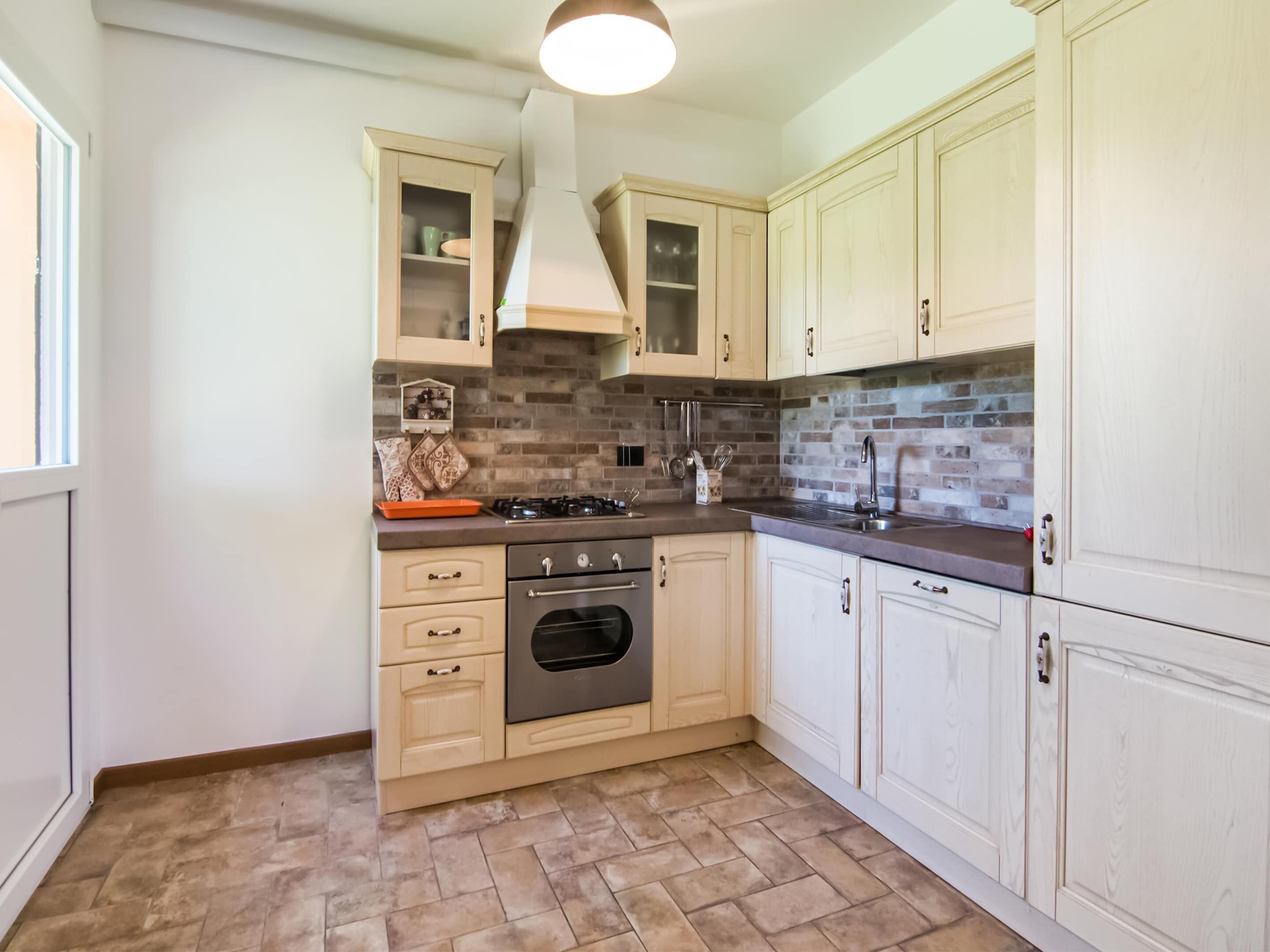 Een keuken met lichte kastjes, een backsplash van baksteen, een gasfornuis en een oven van roestvrij staal.