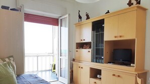 Una stanza con un letto, un mobiletto TV in legno e una televisione, e una porta che dà su un balcone.