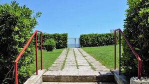 Una serie di gradini in pietra che conducono a un cancello, affiancati da siepi curate e ringhiere rosse.