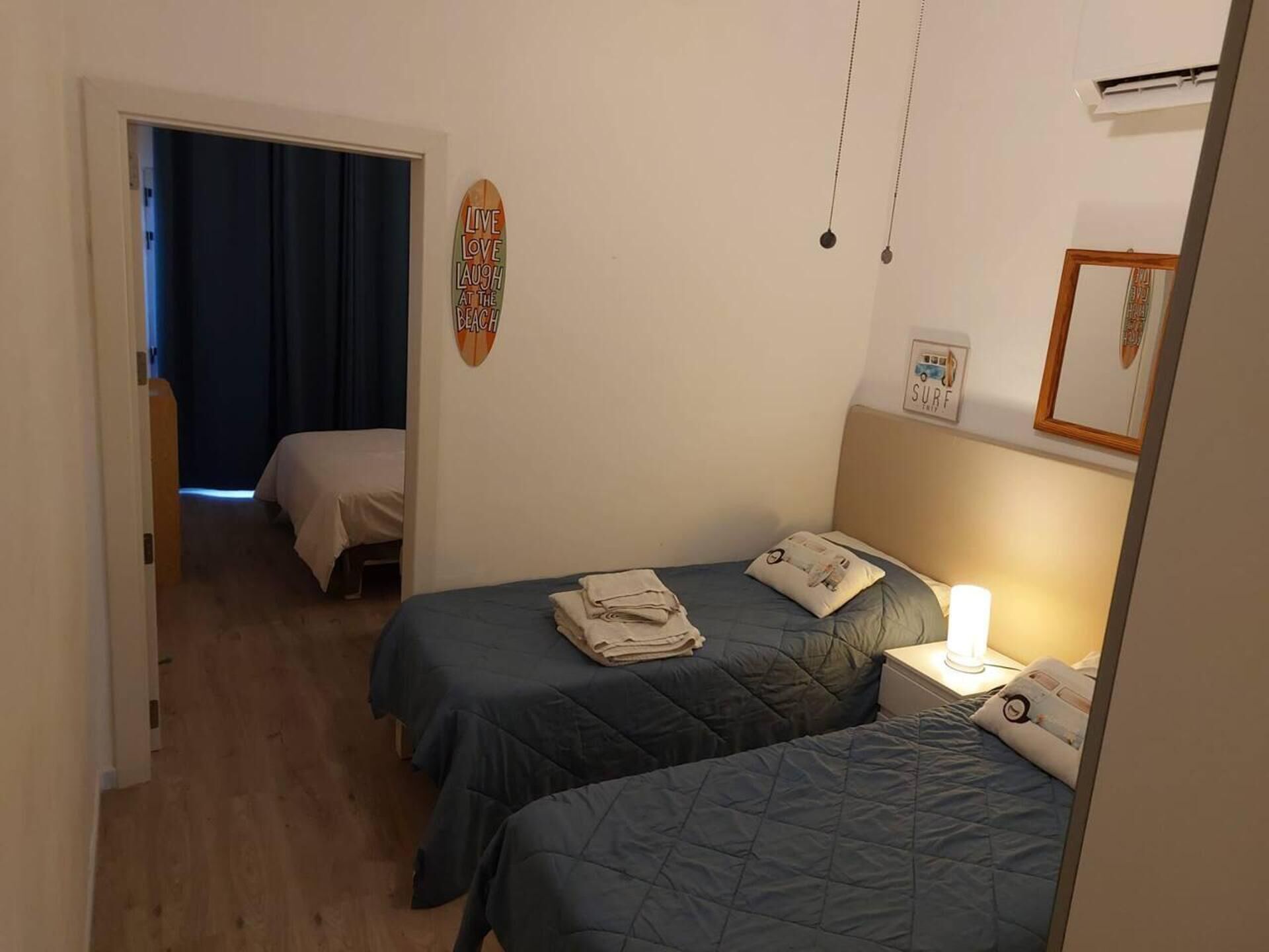 A hotel room with two beds, a door leading to another room, and a wall with a surfboard decoration.