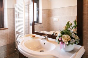 A bathroom with a white sink, a mirror, and a vase of flowers. - Serene Living in a Stone Villa in Marche (Cagli)