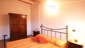 A bedroom with a bed, a wooden wardrobe, a bedside table with a lamp, and a wall-mounted light fixture. - Serene Living in a Stone Villa in Marche (Cagli)