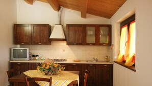 A kitchen with wooden cabinets, a tiled backsplash, a dining table with a yellow tablecloth, and a window with curtains. - Serene Living in a Stone Villa in Marche (Cagli)