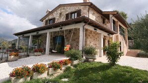 A stone house with a covered porch, outdoor seating, and flower beds. - Serene Living in a Stone Villa in Marche (Cagli)