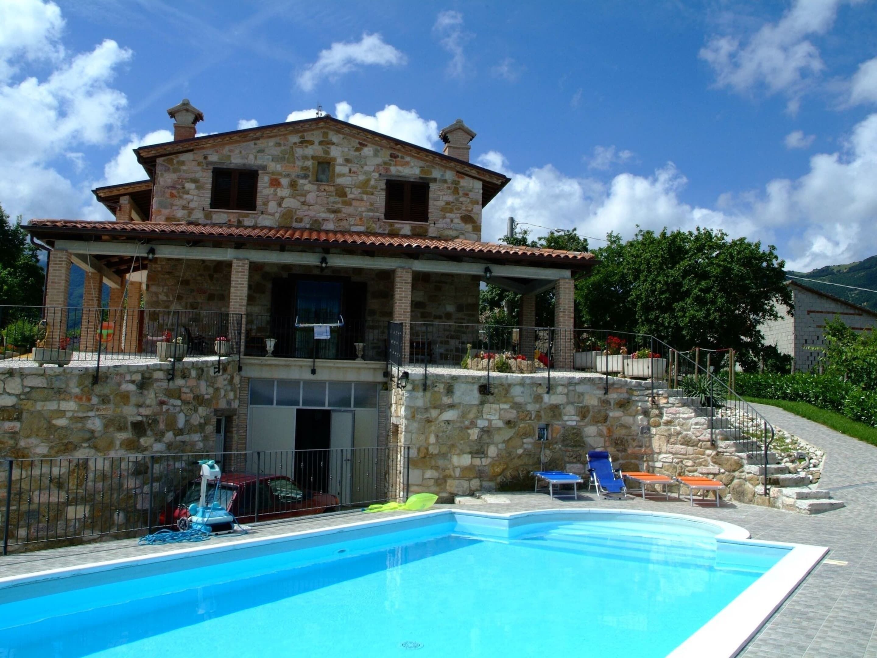 A stone house with a swimming pool, a covered patio, and a stone wall.