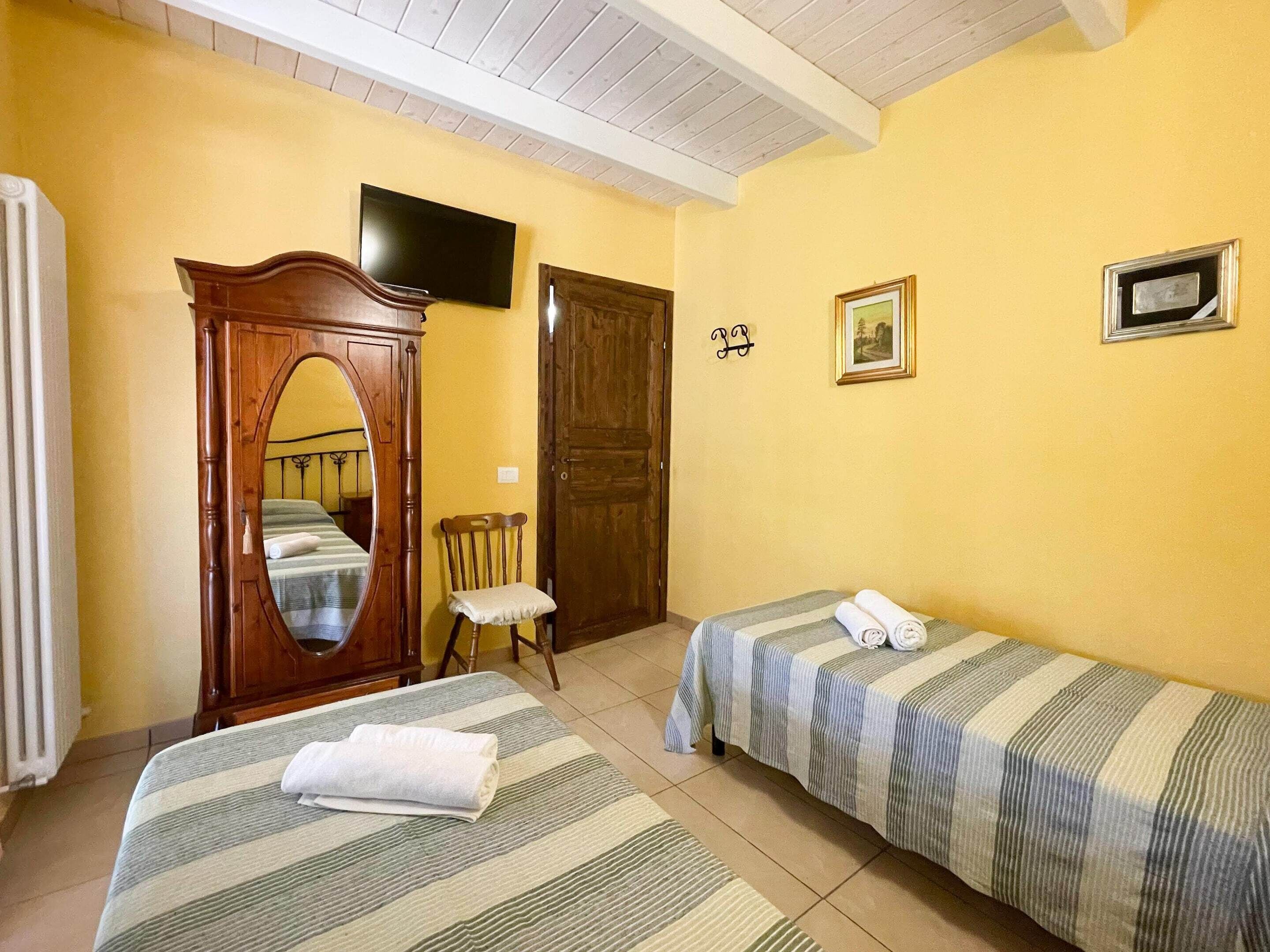A room with two beds, a wooden wardrobe, a chair, a television, and a door.