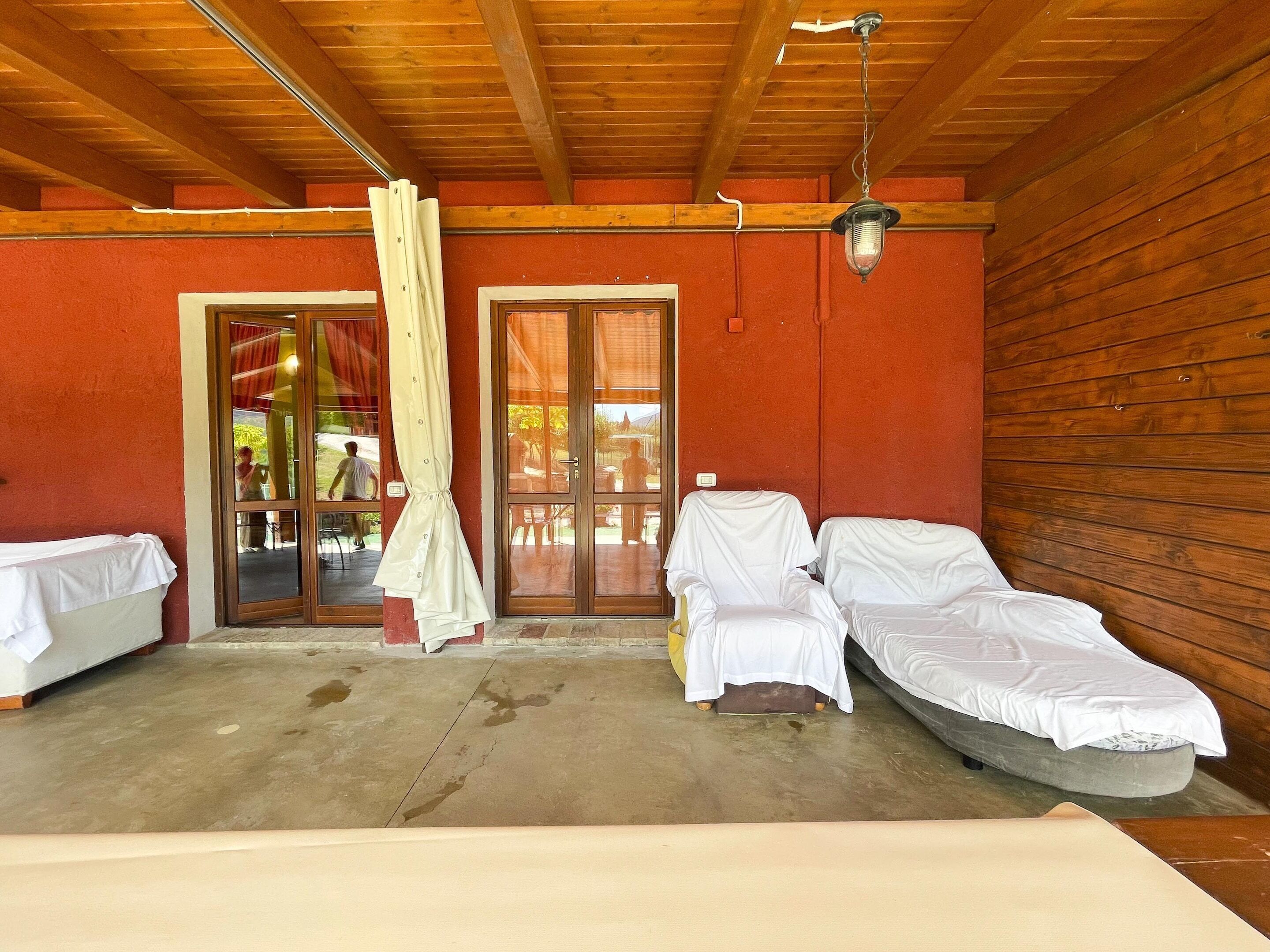 A room with a wooden ceiling, a large sliding glass door, and two beds covered with white sheets.