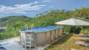 An outdoor swimming pool with a ladder, surrounded by a grassy area and trees, with a view of a forested hill in the background. - Apartment in Massa Marittima With Pool (Massa Marittima)