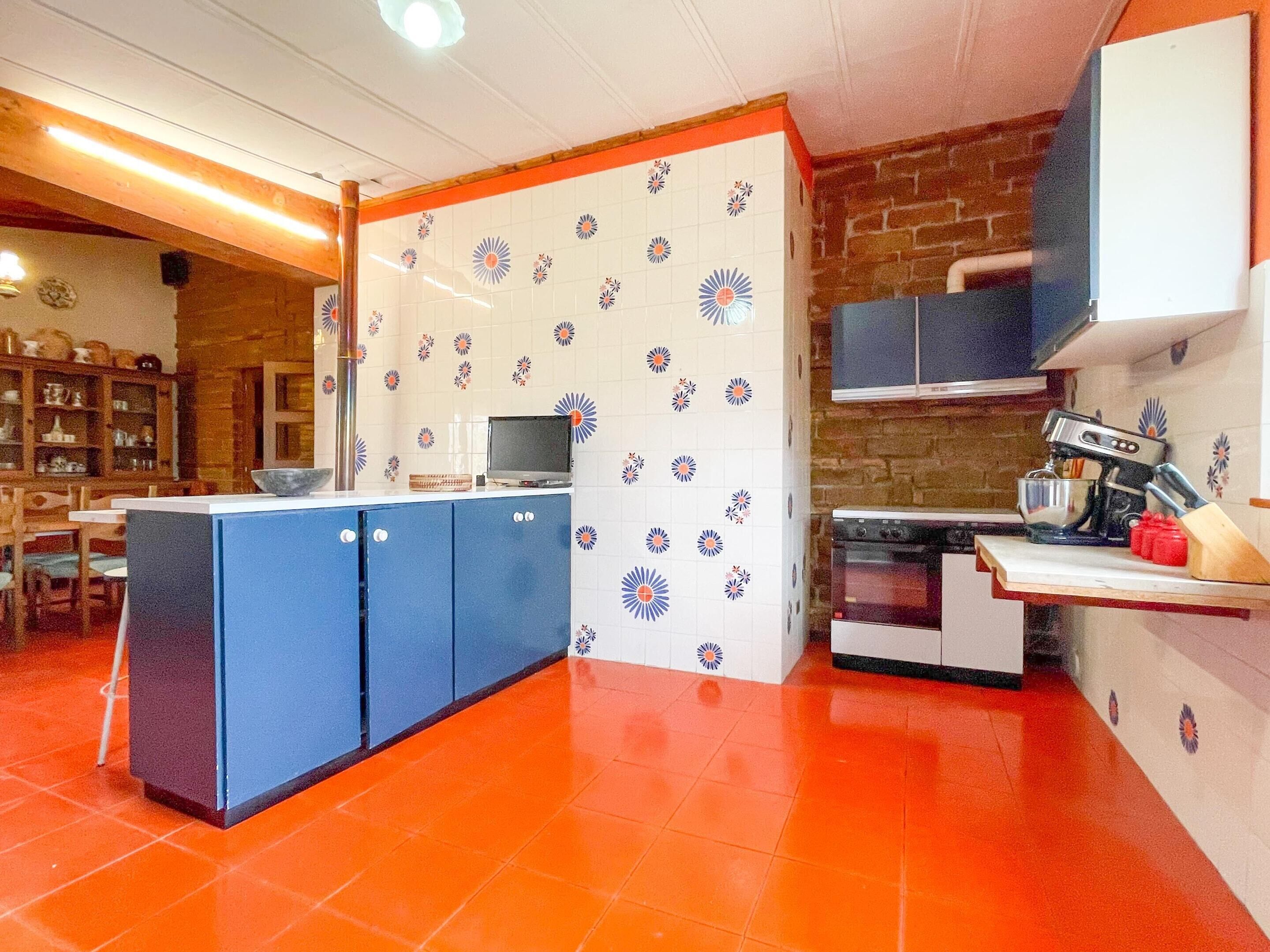 A kitchen with a blue island, white patterned backsplash, and red flooring.