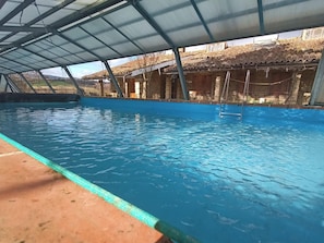 Une piscine dotée d’une zone abritée, entourée de bâtiments en briques et surmontée d’une structure de toit en métal.
