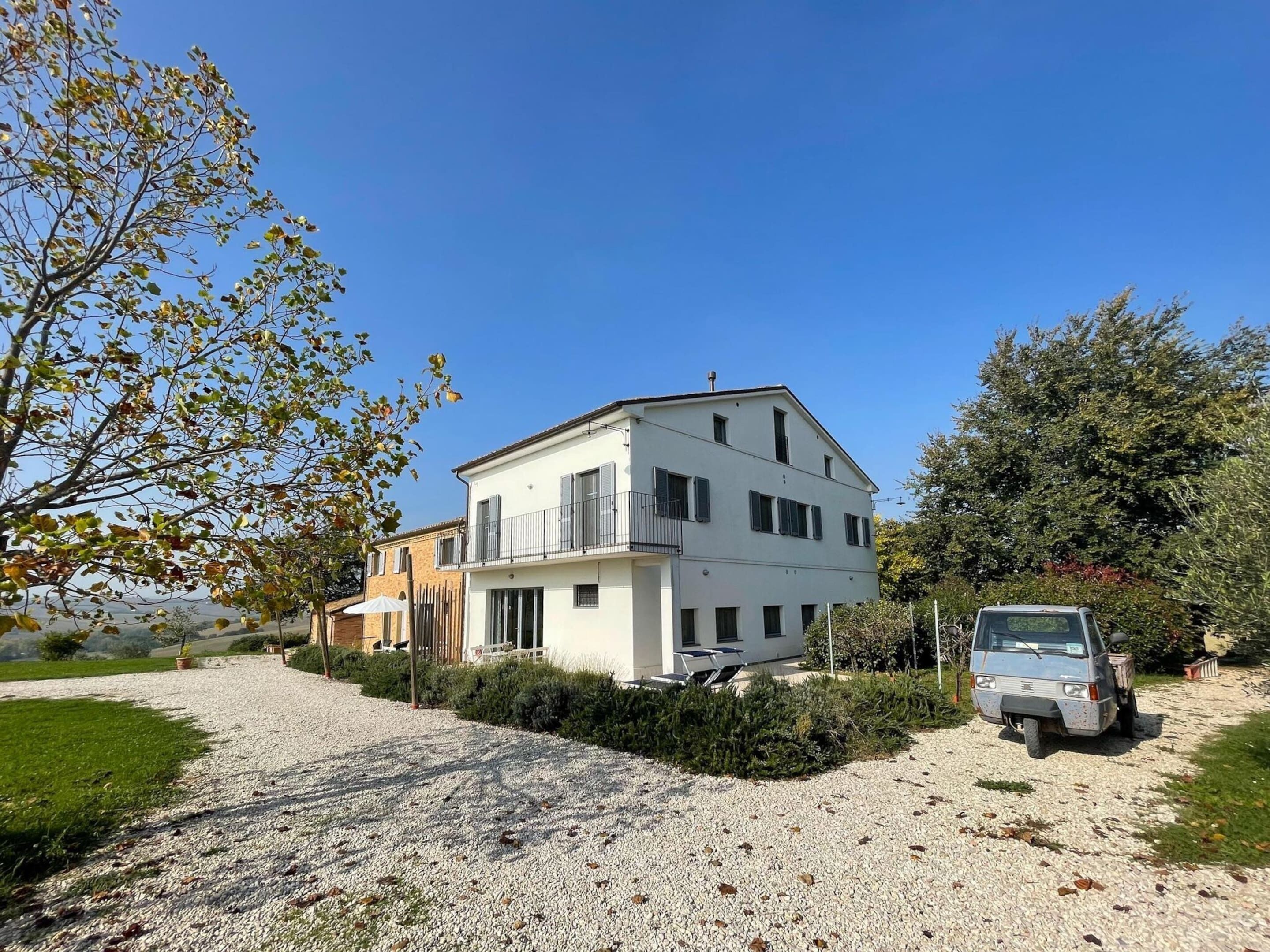 A two-story white house with a gravel driveway and a parked car.