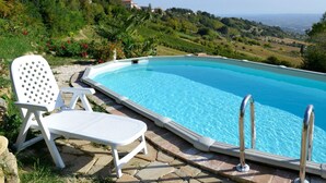 A swimming pool with a clear view of the surrounding landscape, including hills and a distant view of the sea.