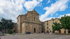 A historic church with a central dome and bell tower, surrounded by a paved square with trees and benches.
