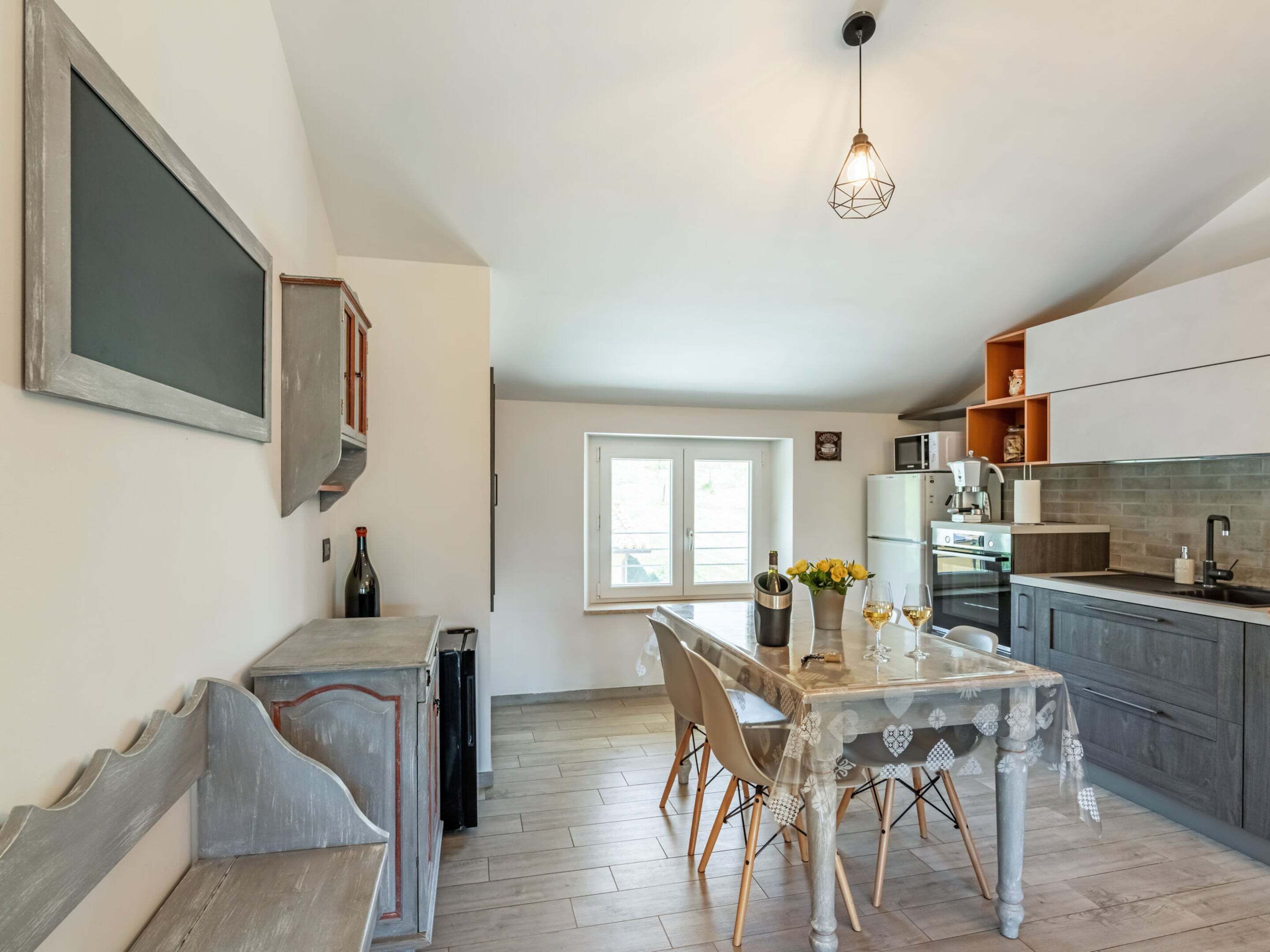 A modern kitchen with a dining area, featuring a table with chairs, a hanging light fixture, and a window providing natural light.