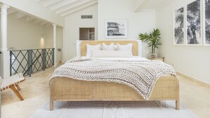 Ein Schlafzimmer mit einem Korbmöbelbett, weißer Bettwäsche und einem großen Fenster.