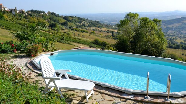 A swimming pool with clear blue water, surrounded by greenery and a view of rolling hills in the background. - Belvilla by OYO Rose di Fratta 1 (Cupramontana)