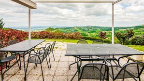 An outdoor patio with tables and chairs, offering a scenic view of rolling hills and a cloudy sky. - Belvilla by OYO Rose di Fratta 1 (Cupramontana)