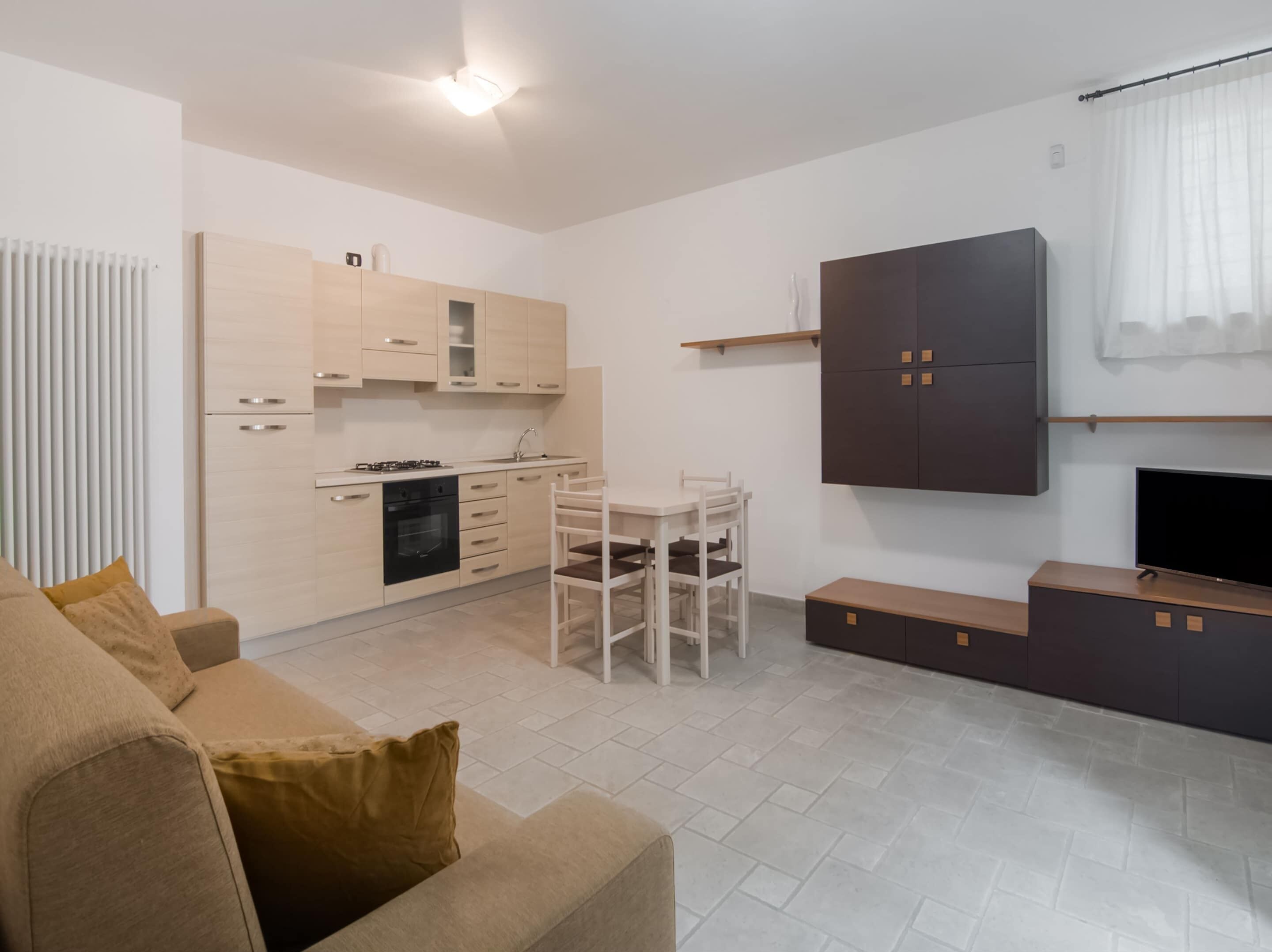 A modern apartment with a kitchenette, dining area, and a living room with a sofa and TV.