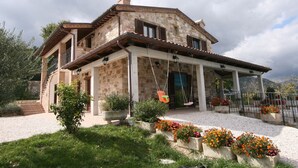 Una casa de piedra con porche cubierto, mobiliario exterior y macizos de flores.