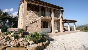Una casa de piedra de dos pisos con un balcón, una escalera y un porche cubierto.