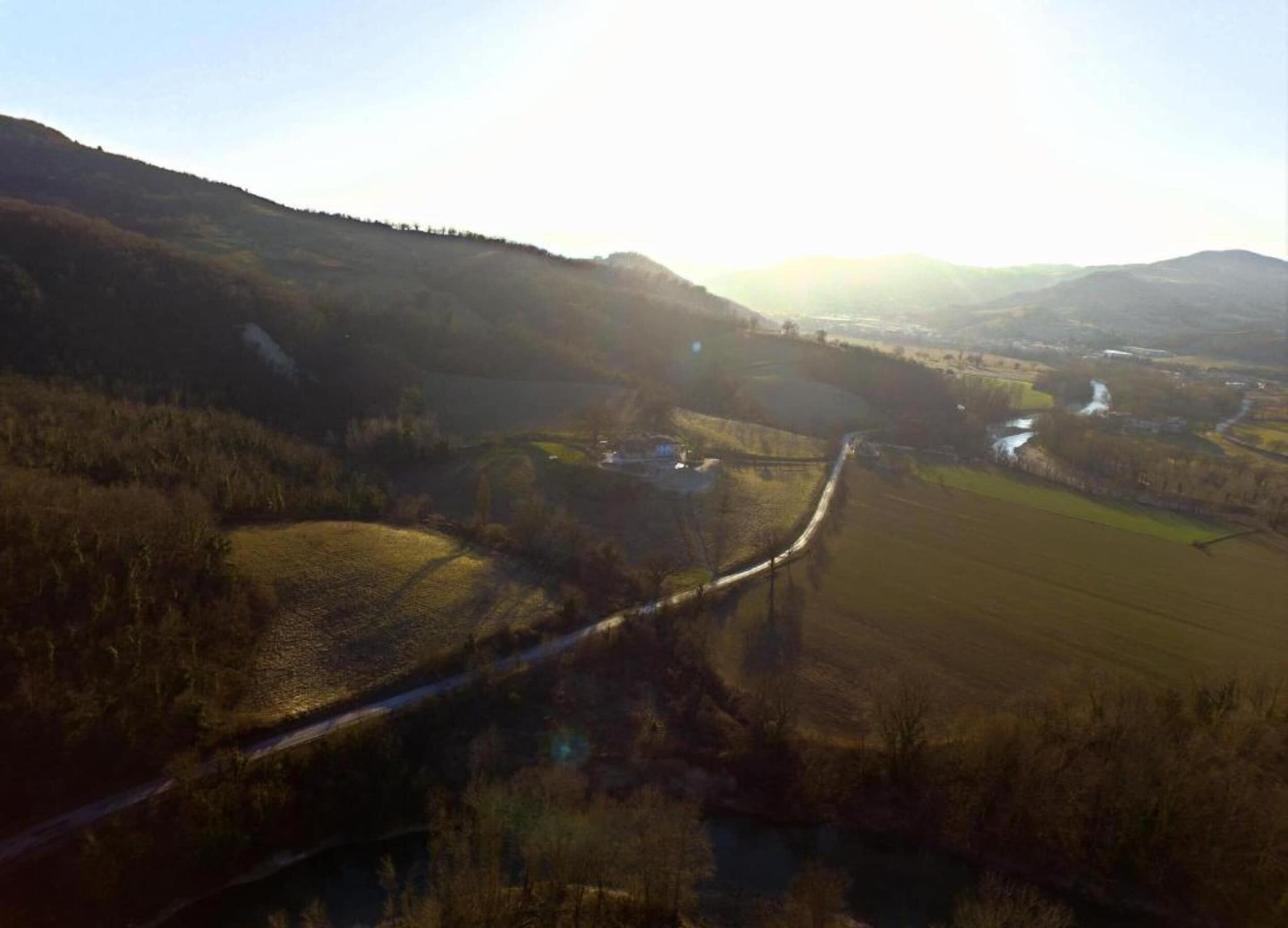 Un paysage rural avec une route sinueuse, des champs et des collines à l’horizon.