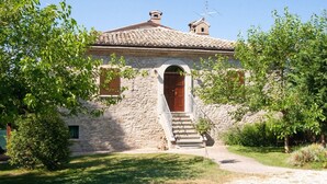 A stone building with a tiled roof, a wooden door, and a staircase leading to the entrance. - Belvilla by OYO Rossini (Urbania)