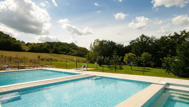 A rectangular swimming pool with two separate sections, surrounded by a grassy area and trees. - Belvilla by OYO Rossini (Urbania)