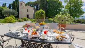 Un espace de restauration en plein air avec une table dressée pour le petit-déjeuner, entourée de chaises, et offrant une vue panoramique sur un paysage pittoresque, avec un bâtiment en arrière-plan.