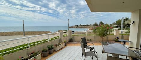 Un balcón con vistas al mar, mobiliario exterior y plantas en macetas.