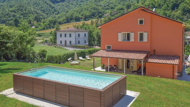 A rectangular swimming pool with a tiled deck, a large house with a red roof and beige walls, and a lush green landscape with hills in the background. - Villa in Borgo Pace With Private Pool (Borgo Pace)