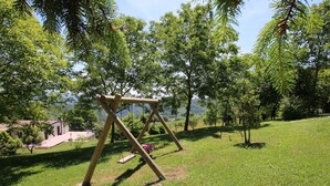 A wooden swing set in a grassy park area with trees and a building in the background. - Farmhouse in Apecchio With Pool & Spa (Apecchio)