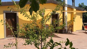 A yellow building with a door and windows, a small patio area with a table and chairs, and a tree in the foreground. - Farmhouse in Apecchio With Pool & Spa (Apecchio)