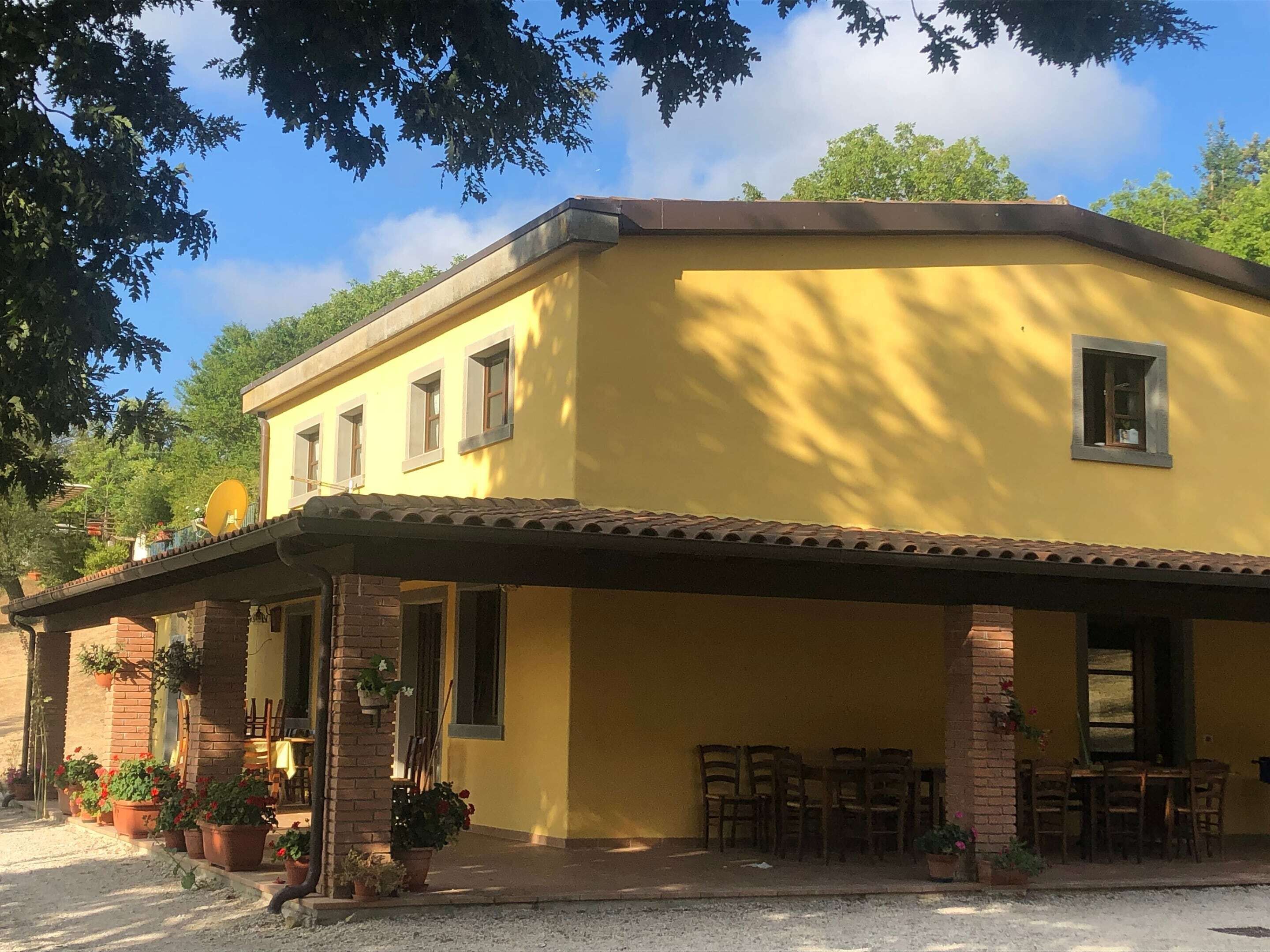 A yellow building with a covered patio, brick pillars, and potted plants.