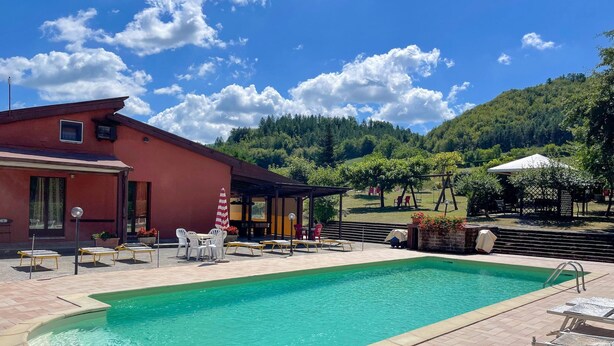 A swimming pool with a tiled deck, outdoor seating, and a view of a forested hillside.