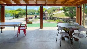 A covered patio area with a table and chairs, a view of a rural landscape, and a stone structure in the background.