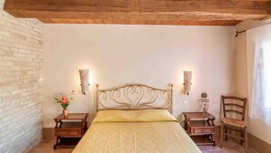 Une chambre avec un plafond en bois, un lit doté d’une tête de lit dorée, deux tables de chevet et une chaise.