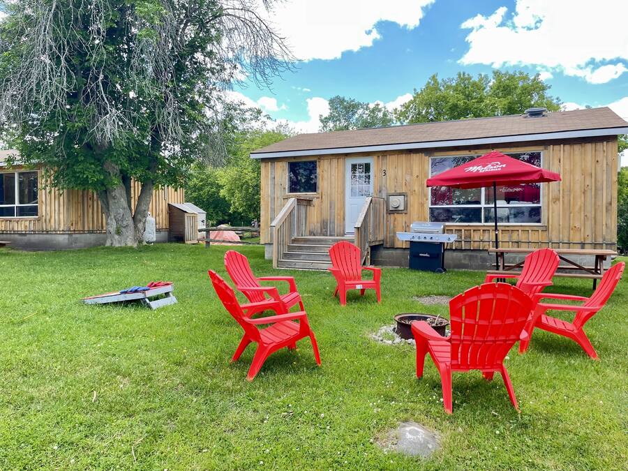 Un edificio de madera con un paraguas rojo, mesas al aire libre y una zona de barbacoa.