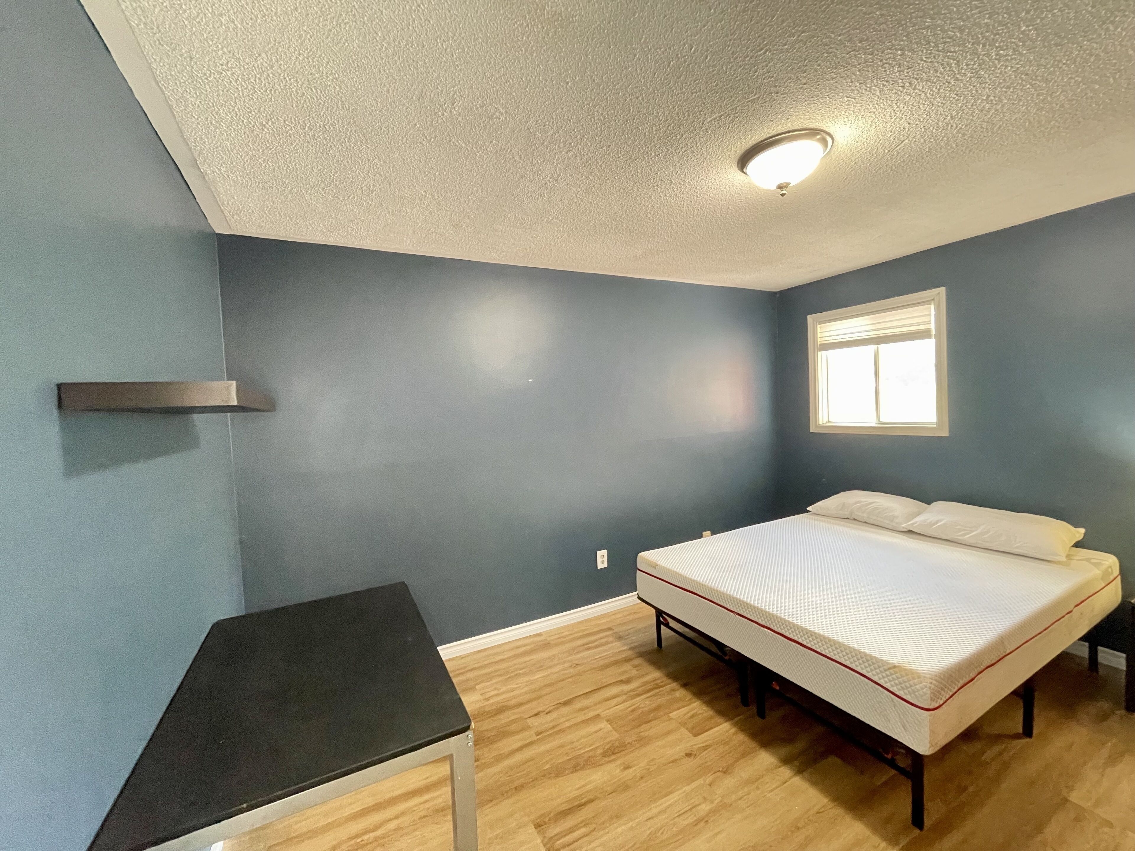 Une chambre à coucher avec un lit, une petite table, une fenêtre et un luminaire au plafond.