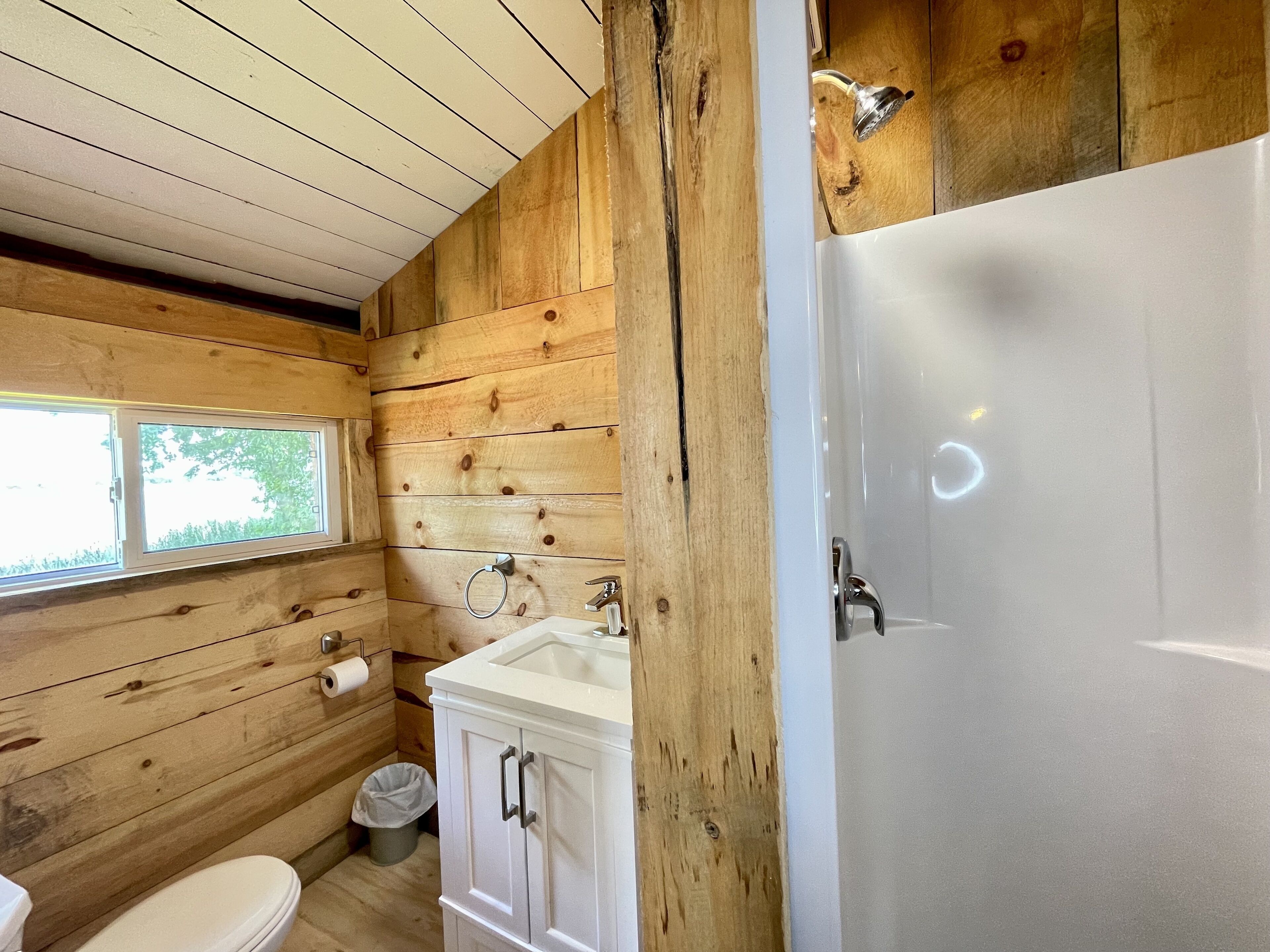 A wooden cabin bathroom with a toilet, sink, and shower.