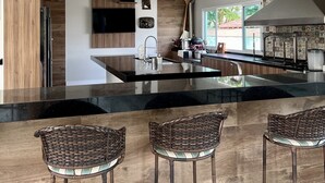 Une cuisine moderne dotée d’un îlot central, de luminaires suspendus et de tabourets de bar en osier.
