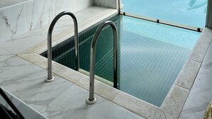 Une salle de bain en marbre avec une piscine à débordement dont l’eau semble s’étendre à l’infini, le tout protégé par des parois de verre.