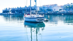 Un voilier est amarré dans une marina, avec des bâtiments en arrière-plan.