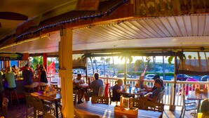 Un restaurant en plein air avec des tables et des chaises en bois, un espace de restauration couvert et une vue sur la rue et les voitures garées.