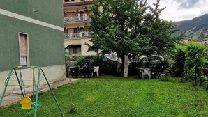 A grassy courtyard with a swing set, a tree, and a building in the background. - Belvilla by OYO Appartamento a Tagliacozzo (Tagliacozzo)