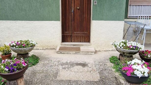 A building with a green and white facade, a wooden double door, and a small porch area with potted plants. - Belvilla by OYO Appartamento a Tagliacozzo (Tagliacozzo)