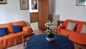 A room with two orange sofas, a round table with a blue tablecloth, and a potted plant with white flowers. - Belvilla by OYO Appartamento a Tagliacozzo (Tagliacozzo)
