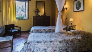 A bedroom with two beds, a wooden chair, a dresser, a window with curtains, a bedside table with a lamp, and a wall-mounted mirror. - Chalet in Monte Sibillini Park (Amandola)